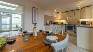 Una cocina moderna con armarios blancos, una mesa de comedor dispuesta con copas de vino y una botella, y vistas al exterior a través de amplios ventanales.