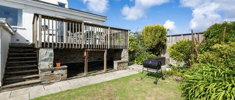 A modern house with a wooden deck, a stone staircase, and a barbecue grill in the yard.