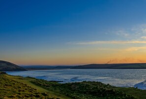 A coastal landscape with a grassy foreground and a view of the sea and distant hills.