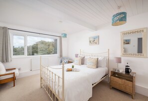 A bedroom with a bed, bedside table, and a window with curtains. - Palm Trees is located in a quiet setting to the rear of Westwood Flats. (Wadebridge)