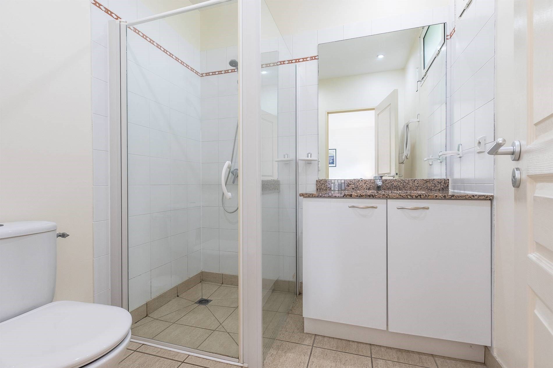 A bathroom with a glass-enclosed shower, a toilet, and a vanity with a mirror.