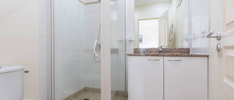 A bathroom with a glass-enclosed shower, a toilet, and a vanity with a mirror.