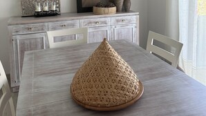 Una mesa de comedor con un centro de mimbre, una obra de arte enmarcada arriba y un objeto decorativo en el aparador.