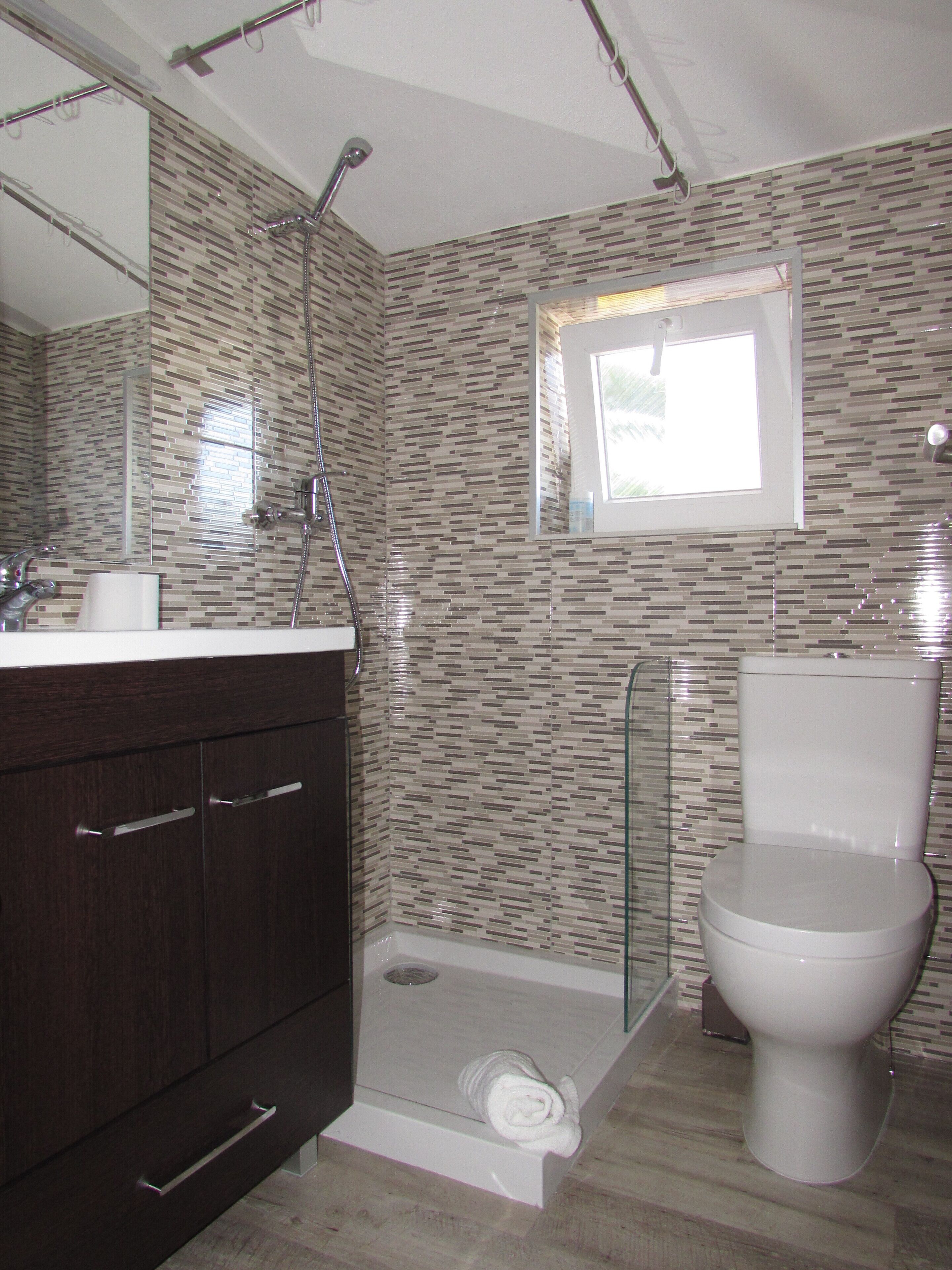 A bathroom with a shower, toilet, and dark wooden cabinet.