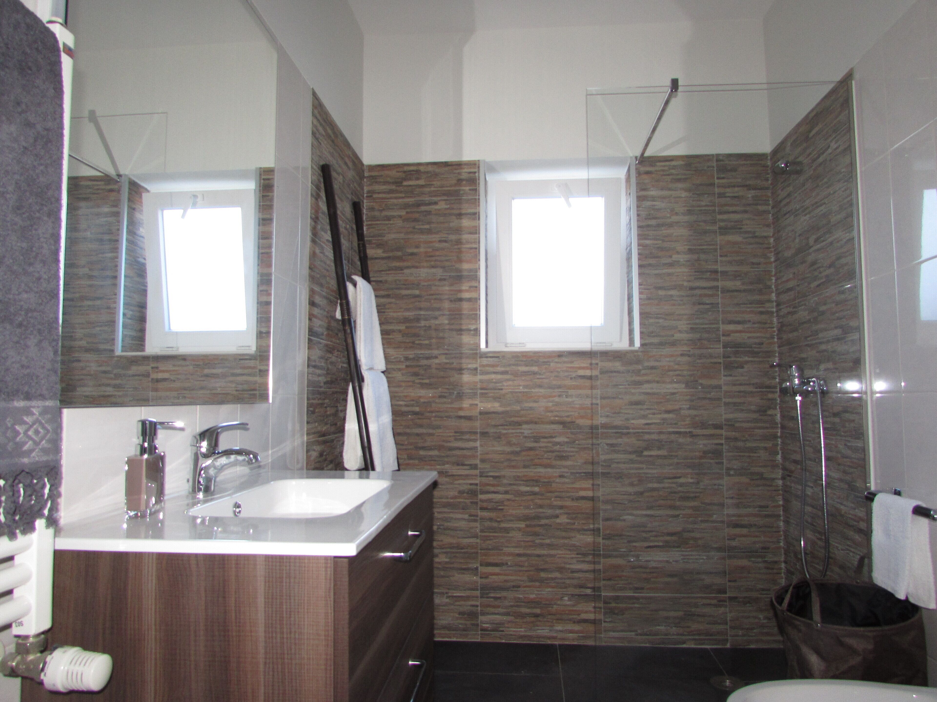 A modern bathroom with a wooden vanity, a glass shower enclosure, and two small windows.