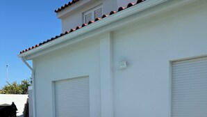 Un edificio blanco con techo de tejas, dos grandes macetas de terracota y una zona pavimentada con piedra.
