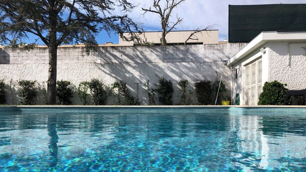 Una piscina transparente con borde de azulejos, rodeada por un muro de concreto y vegetación.