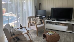 Una sala de estar moderna con un televisor de pantalla plana, dos sillones, una mesa de centro y un ventanal con cortinas.