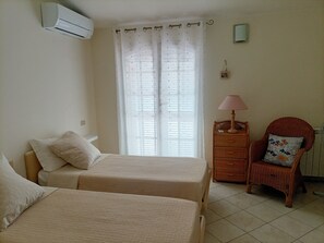 Une chambre avec deux lits, une chaise, une table de chevet avec une lampe et une fenêtre avec des stores.