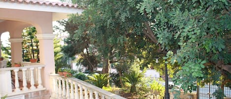 A stone balustrade leading to a covered area with potted plants and trees.