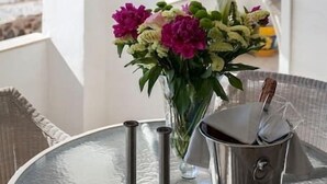 Een tafel met een bloemenvaas, een kandelaar, en een emmer met een kaars in een kamer met uitzicht op het strand en de zee.