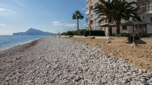 Een kiezelstrand met een gebouw voorzien van balkons en palmbomen.