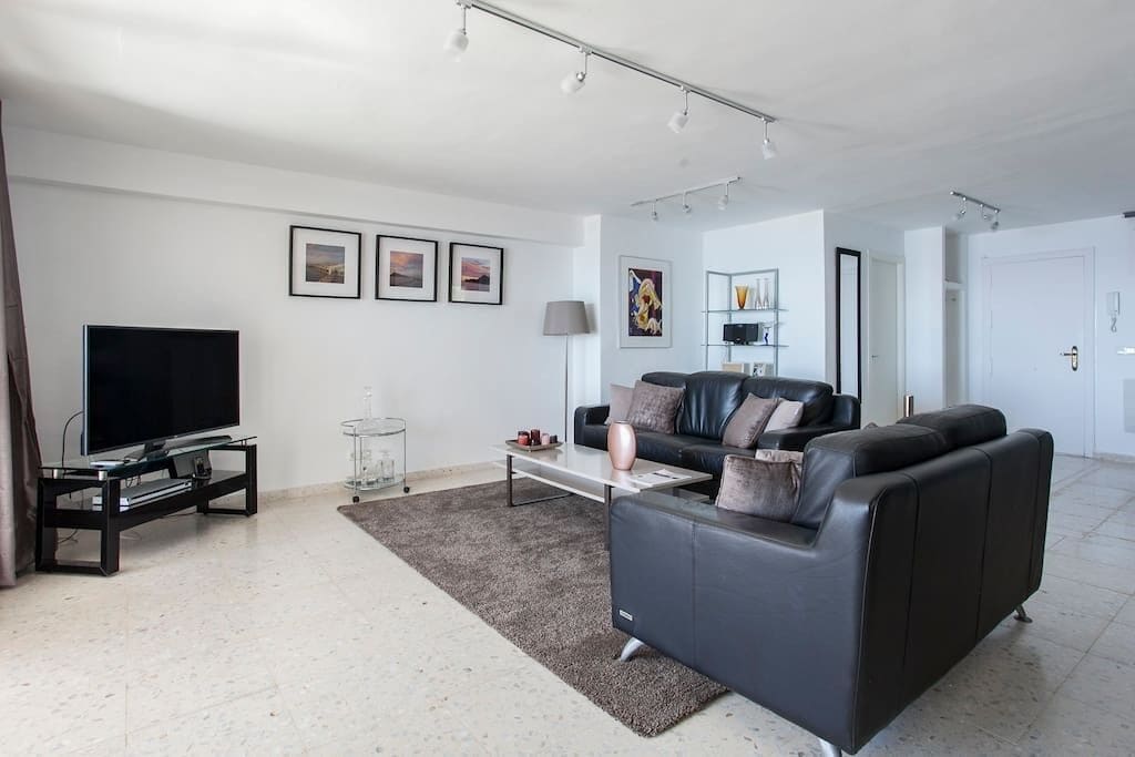 Una sala de estar moderna con un televisor de pantalla plana, un sofá de cuero negro, una mesa de centro y una alfombra.