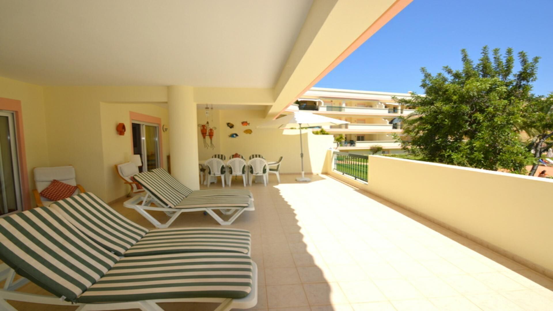 A balcony with two striped lounge chairs, a small table with chairs, and a view of a building and trees.