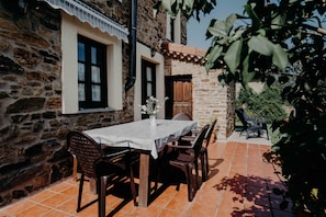 A stone building with a tiled patio, a table with chairs, and a potted plant.