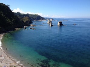 Un paisaje costero con aguas cristalinas, afloramientos rocosos y una playa.