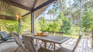 A wooden deck with a table and chairs, surrounded by trees. - Villa Spacieuse et Moderne Avec Piscine Privée! (Moliets-et-Maa)