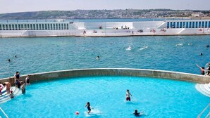 A swimming pool area with multiple pools, a viewing deck, and a cityscape in the background.
