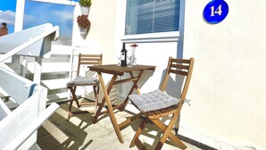 A balcony with two wooden chairs and a table, a potted plant, and a window with blinds.