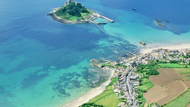 An aerial view of a coastal town with a prominent island featuring a castle-like structure, connected by a bridge.