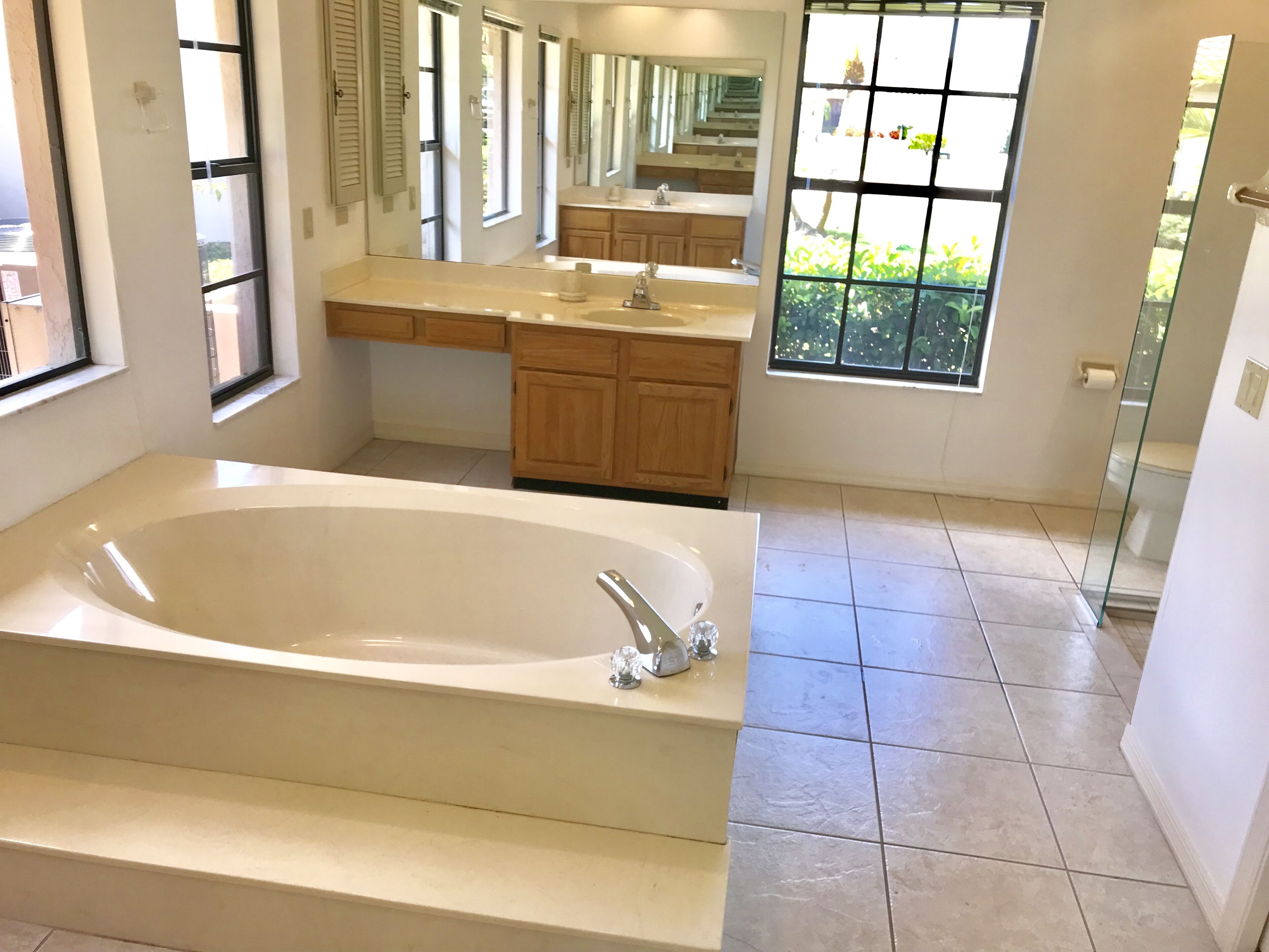 A modern bathroom with a large bathtub, wooden cabinets, a vanity with a mirror, and a window with a view of greenery.
