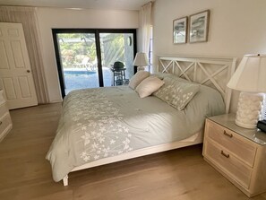 A bedroom with a bed, a bedside table, a lamp, and a view of an outdoor area.
