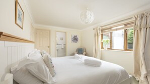 Un lit bien fait, avec des oreillers et une serviette enroulée, une tête de lit en bois, un luminaire blanc au plafond et une fenêtre avec des rideaux.