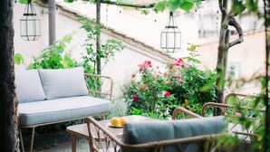 Un área de estar exterior de mimbre con un sofá y sillas, rodeada de follaje y flores.