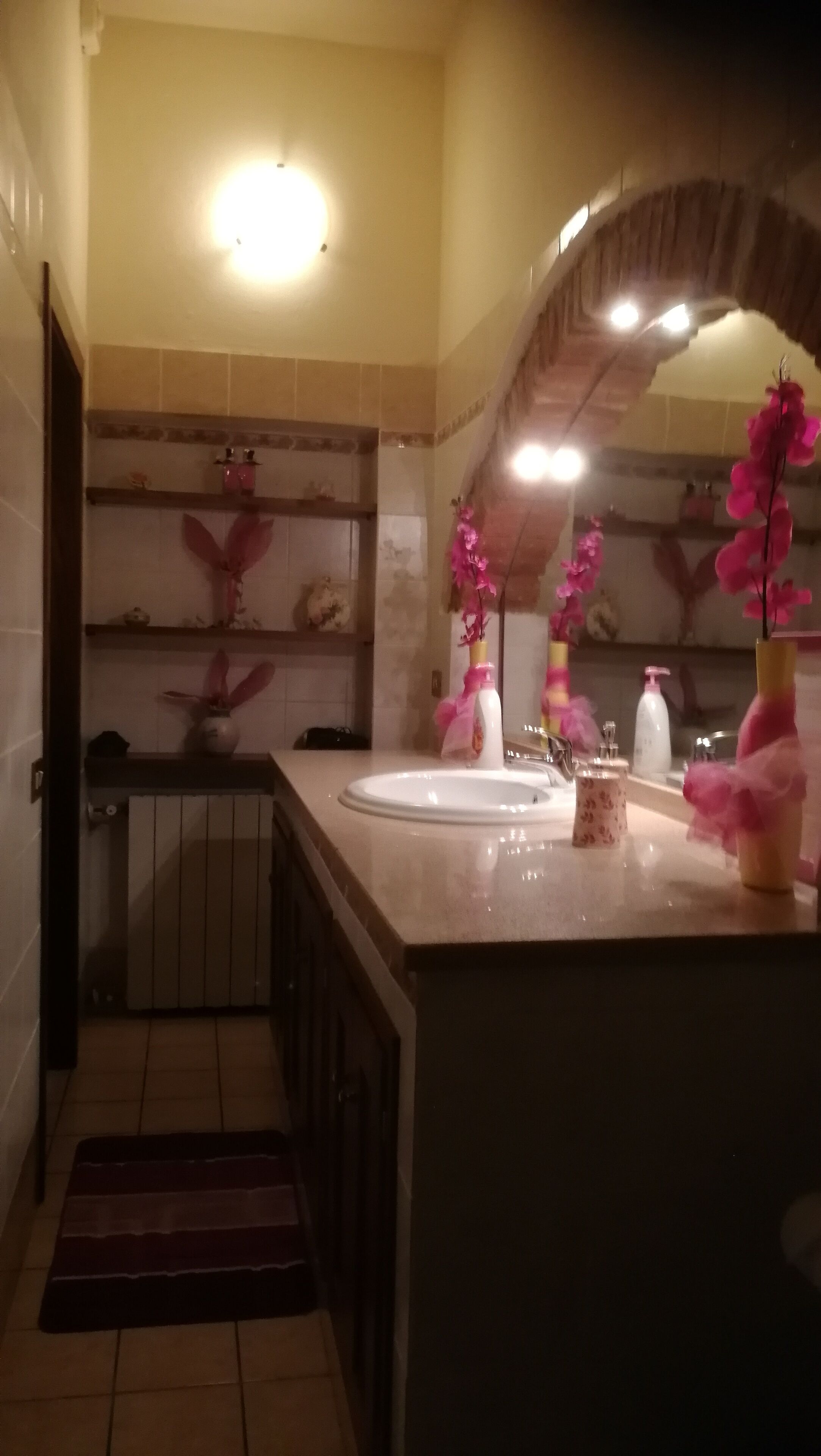 A bathroom with a sink, mirror, and decorative flowers. There is a towel rack and a shower area visible.
