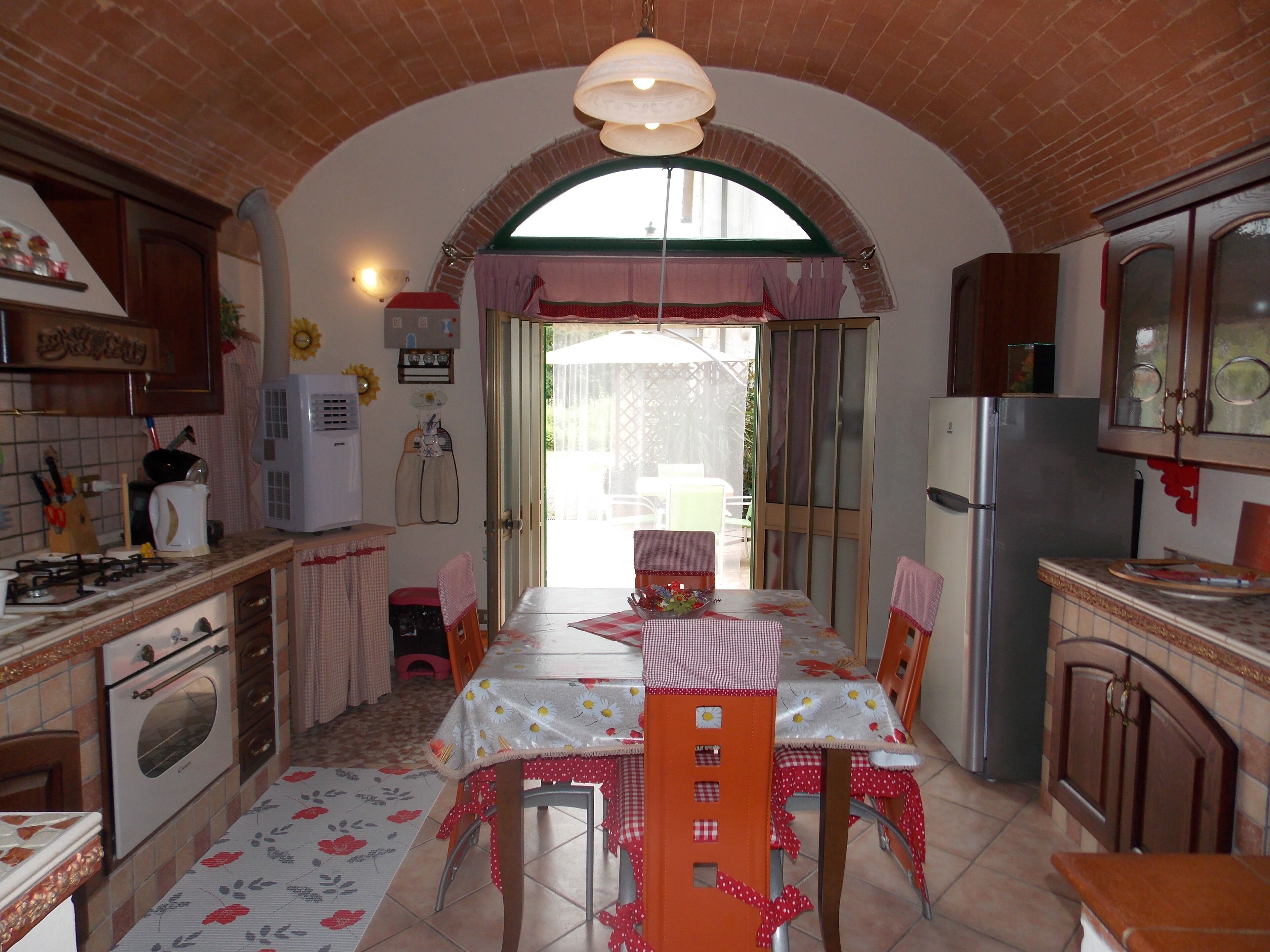 Une cuisine avec un plafond en arc de cercle, une table à manger avec des chaises et un réfrigérateur.