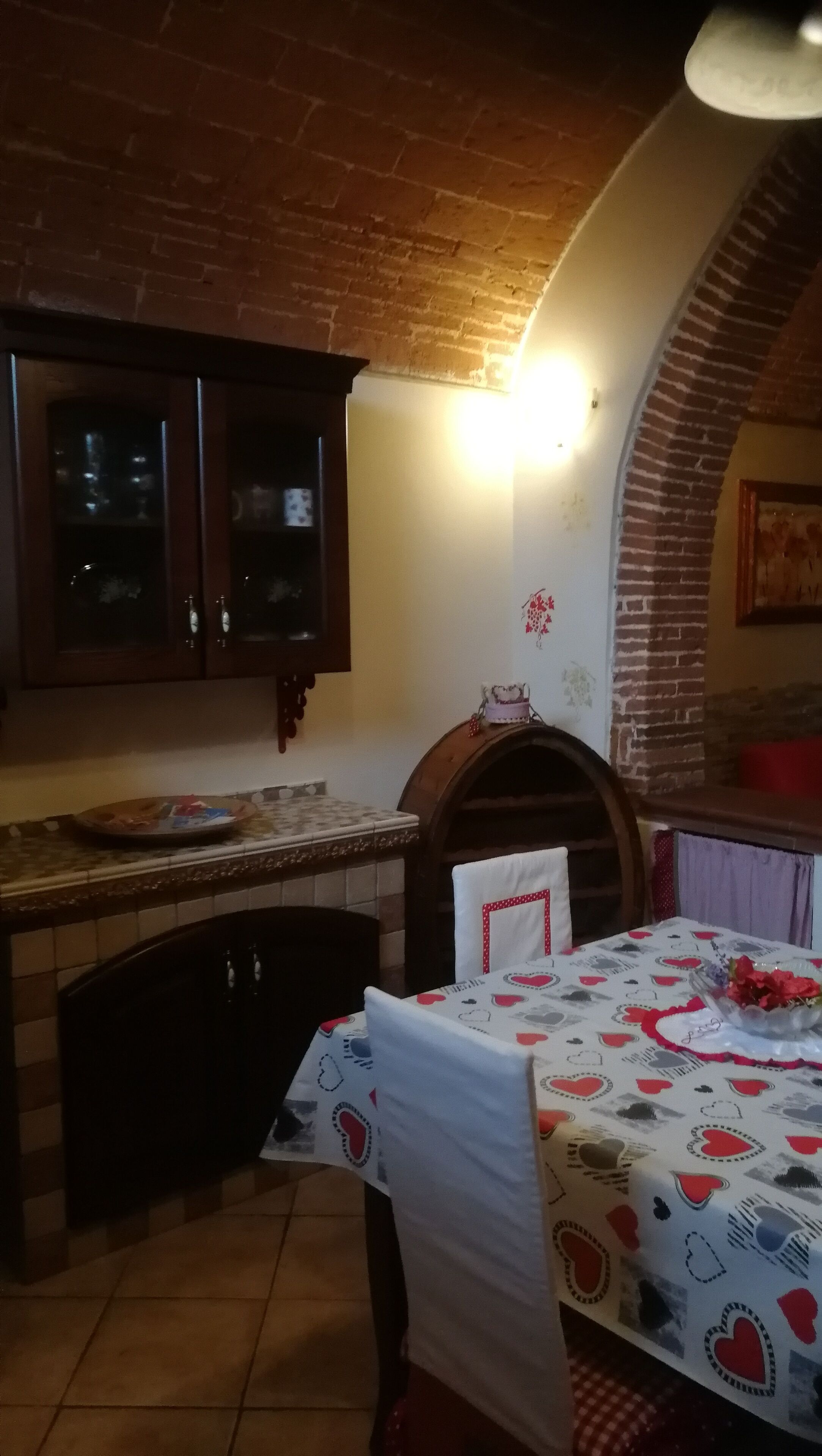 A dining area with a brick fireplace, a table set with a heart-patterned tablecloth, and a cabinet with glass doors.