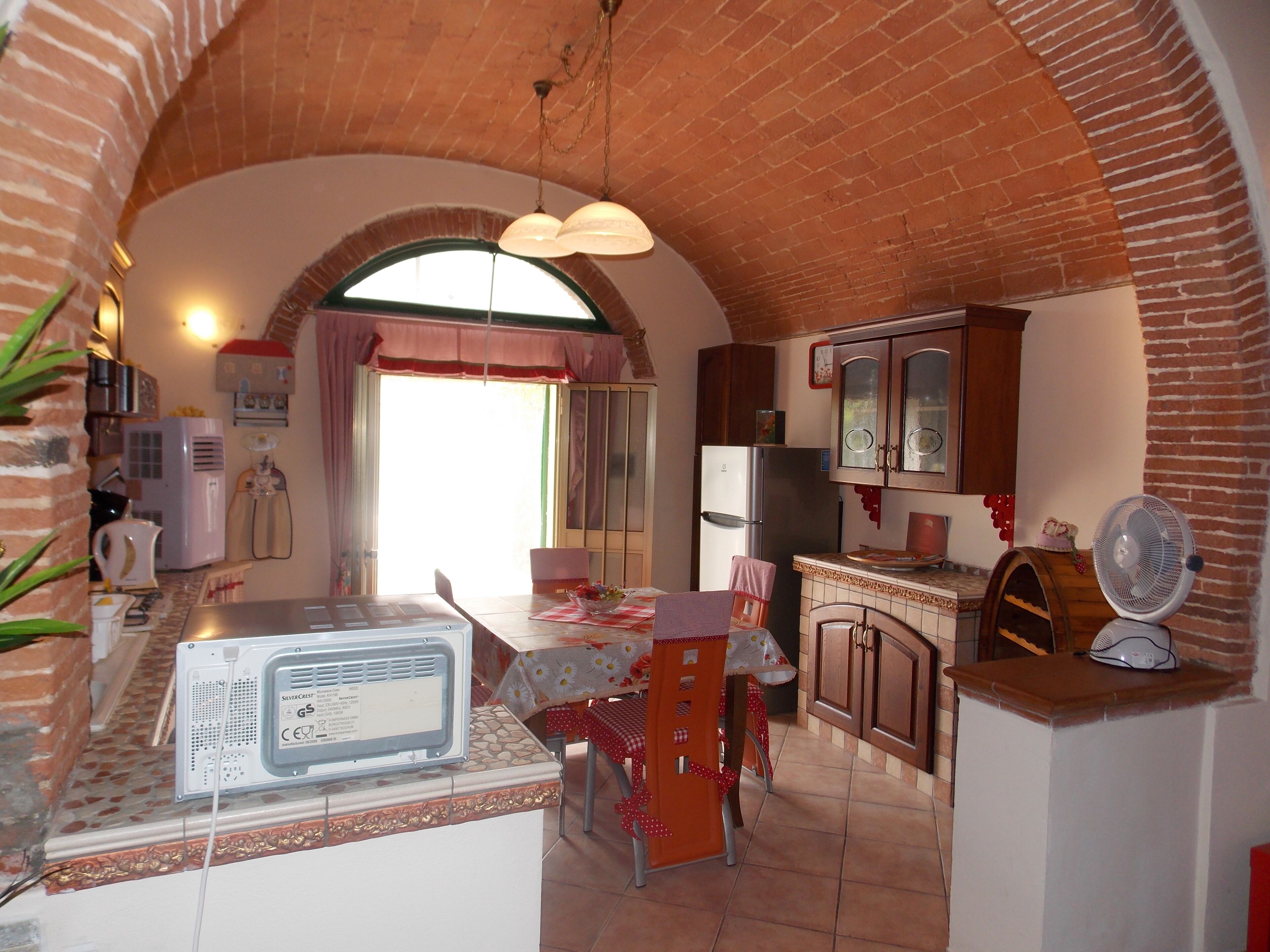 A compact kitchen with a brick arch, a refrigerator, a microwave, and a dining area with a table and chairs.