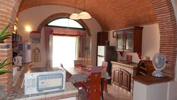 A compact kitchen with a brick arch, a refrigerator, a microwave, and a dining area with a table and chairs.