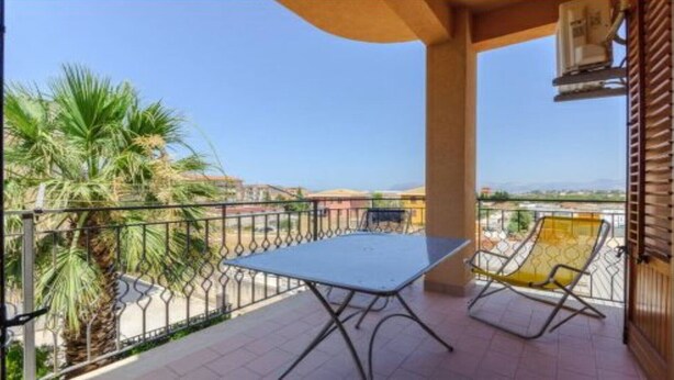 A balcony with a table and two chairs, a palm tree, and a view of buildings and mountains. - apartment near the sea (scoppello Guidaloca) (Castellammare del Golfo)