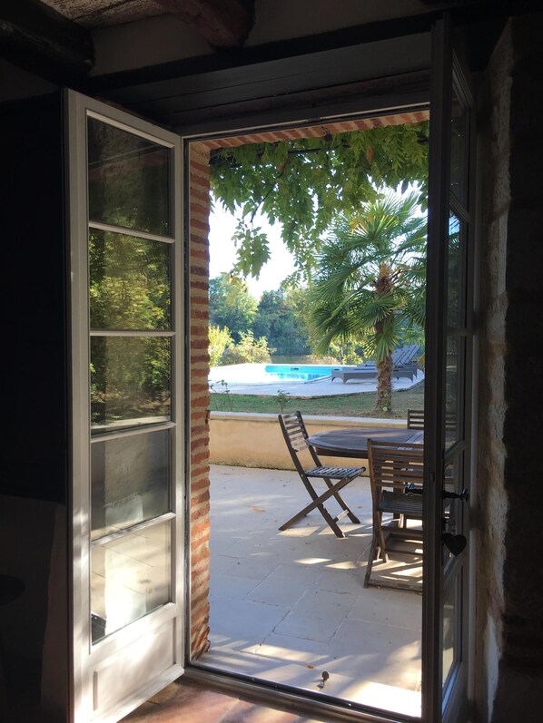 A sliding glass door leading to an outdoor patio area with a pool, a palm tree, and a wooden table and chairs.