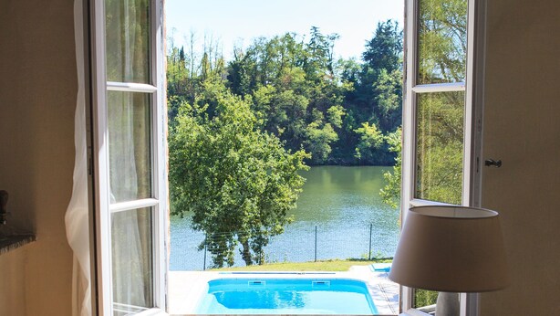A room with a view of a lake and a swimming pool through an open window. - Beautiful Cottage ****  on the bank of the river Tarn - 6/7 people. Pool . (Labastide de Levis)