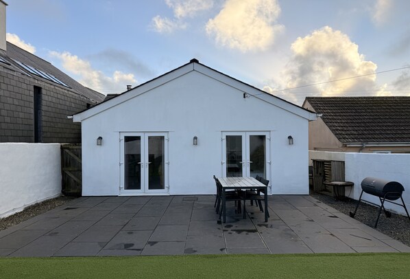 A white house with a tiled patio, a table and chairs, and a barbecue grill. - Miss Fishers is a charming two bedroom cottage close to Port Isaac. (Port Isaac)