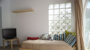Ein Schlafzimmer mit einem Bett, einem Fernsehgerät auf einem Standfuß, einem Fenster mit Dekorglas und einem Regal über dem Bett.