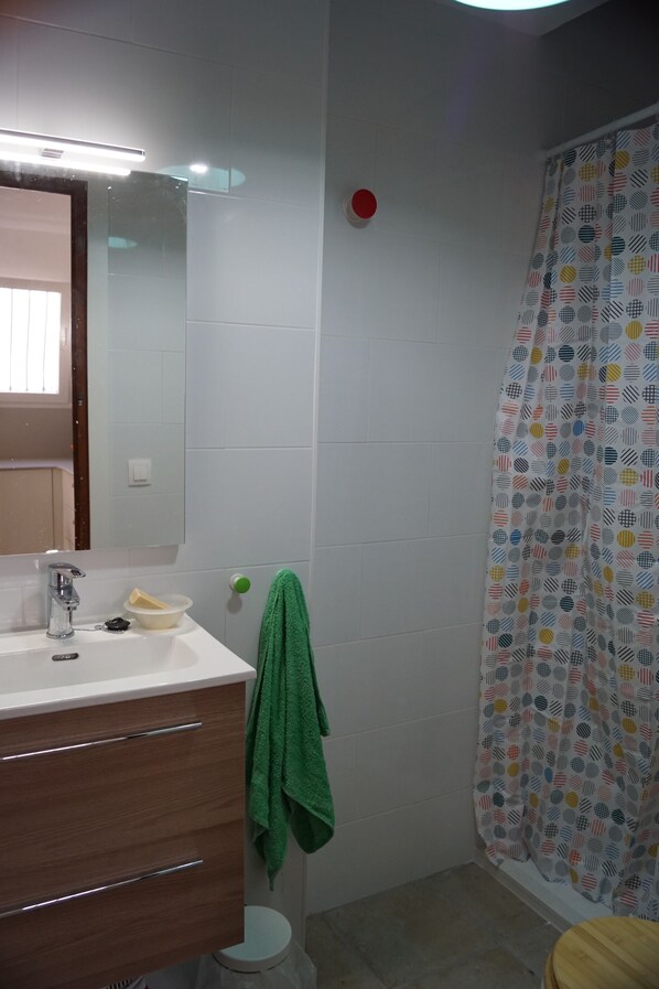 Un baño con lavamanos blanco, espejo y toalla verde.