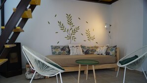 Ein gemütlicher Raum mit einer Couch, zwei weißen Stühlen, einem kleinen Tisch und einer Wand mit Blattschablonen.