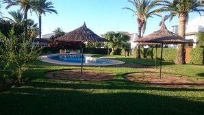 Ein Poolbereich mit zwei Reetsonnenhüten, einem runden Pool und umgebender Bepflanzung.