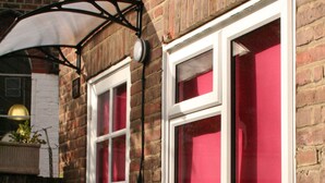 A brick house with a white door and windows, a small porch, and a red curtain on the windows. - Self-contained New Studio with independent entrance in an up-market quiet area. (London)
