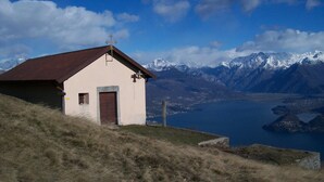 Un piccolo edificio a un piano con tetto spiovente, una porta e una finestra. Si trova su una collinetta erbosa con vista su un lago e montagne innevate sullo sfondo.
