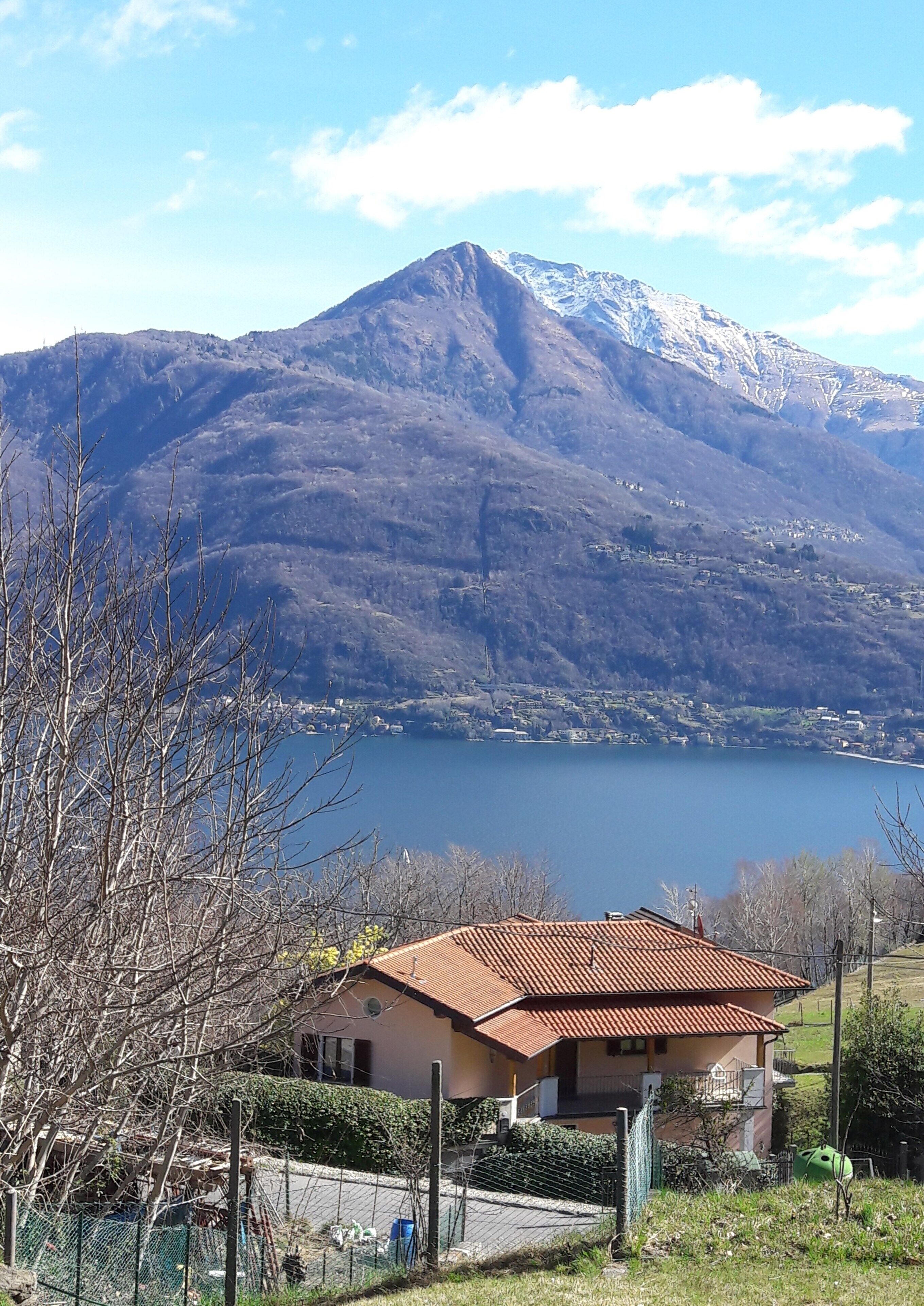 Une maison avec un toit rouge, une cour clôturée et une montagne en arrière-plan.