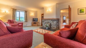 A living room with red sofas, a stone fireplace, a television, and a view of the outdoors. - September is a lovely spacious house in the heart of Roserrow. (Wadebridge)