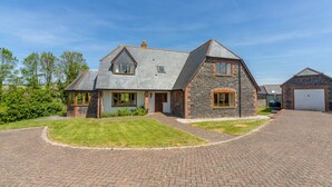 A two-story house with a stone facade, a brick driveway, and a well-maintained lawn. - September is a lovely spacious house in the heart of Roserrow. (Wadebridge)