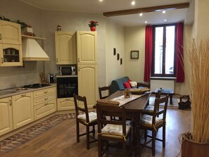 A compact kitchen with a dining area, wooden cabinets, a microwave, and a clock on the wall. - Lovely apartment in Cuneo Center (Cuneo)
