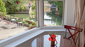A room with a large window overlooking a canal, a round glass table with a vase of flowers, and a wooden chair. - Luxury Studio with balcony over the River Thames in historic centre of Oxford (Oxford)