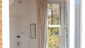 A room with a bed, a window with curtains, a table with chairs, and a door. - Luxury Studio with balcony over the River Thames in historic centre of Oxford (Oxford)