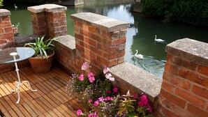 A wooden deck with a glass table and chairs, surrounded by brick walls and a water feature with swans. - Luxury Studio with balcony over the River Thames in historic centre of Oxford (Oxford)
